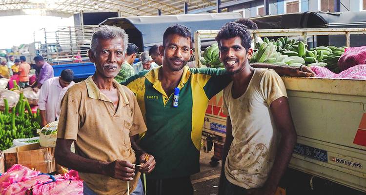 Trois hommes posant joyeusement dans un environnement de marché avec des produits frais.