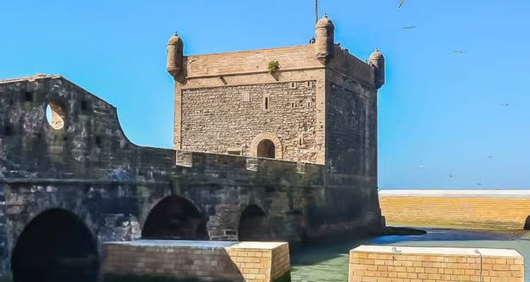 Una fortaleza de piedra junto al agua bajo un cielo azul despejado.