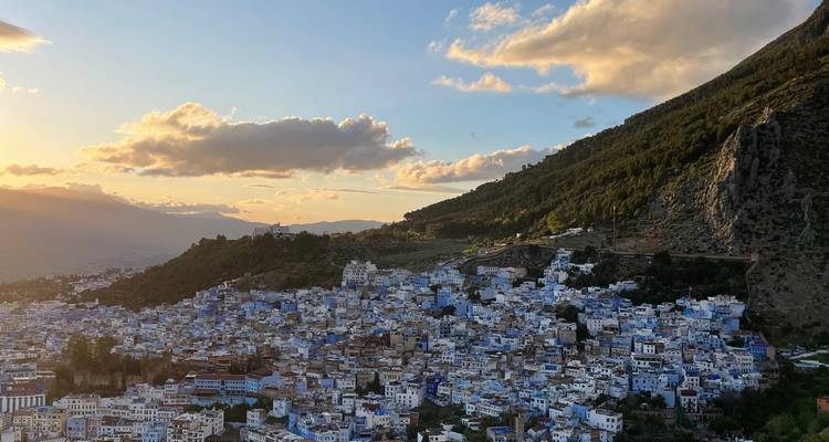 Un pueblo en la ladera pintado de azul, con un telón de fondo montañoso al atardecer.