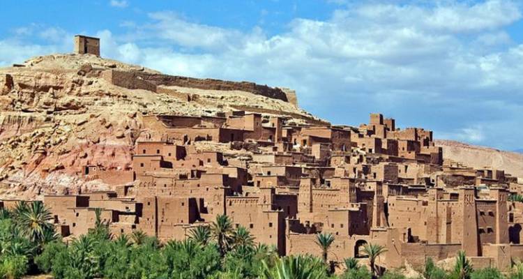 A historic clay settlement on a hill with palm trees in the foreground.
