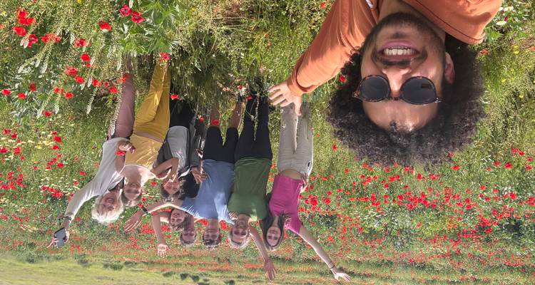 Smiling guide takes selfie with group amid vibrant field of red poppies on a sunny day.