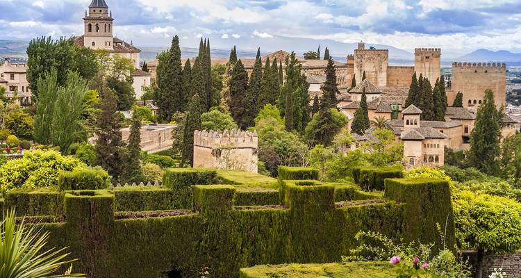 Les jardins luxuriants et les murs historiques du complexe de l'Alhambra se dressant contre des nuages dramatiques à Grenade.