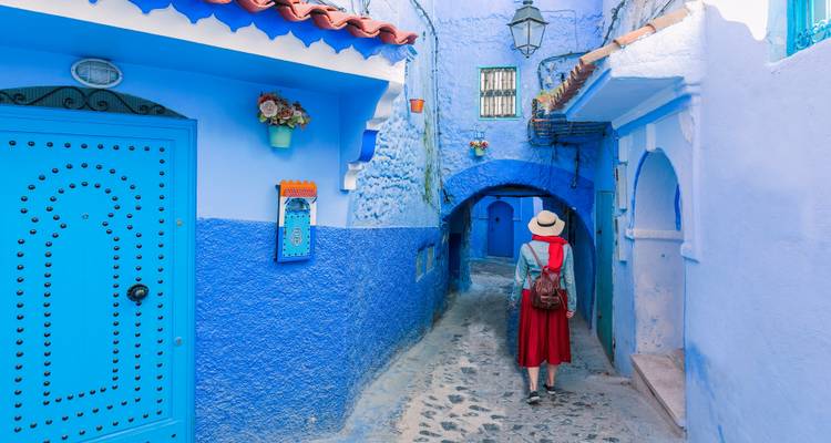 Frau, die in traditioneller Kleidung durch eine lebendige blaue Gasse geht.