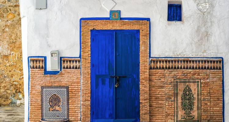 Blauw geverfde deur met decoratieve tegels op een bakstenen muur.
