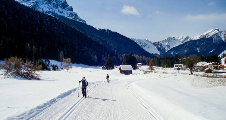 Les skieurs de fond glissent le long d'une piste enneigée fraîchement damée, entourée de pics alpins et de forêts de conifères