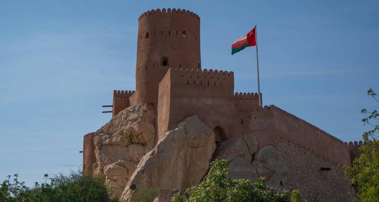 Forteresse avec drapeau au sommet d'une colline sous un ciel dégagé.