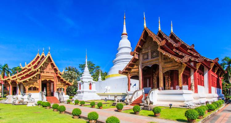 Complexe de temples avec architecture traditionnelle thaïlandaise et stupa sous un ciel bleu dégagé.