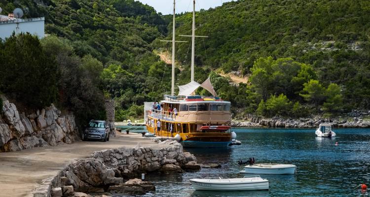 Scène côtière avec un bateau amarré près de formations rocheuses et de verdure.