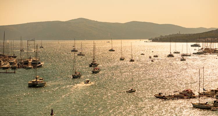 Voiliers sur une mer scintillante avec des montagnes en arrière-plan.