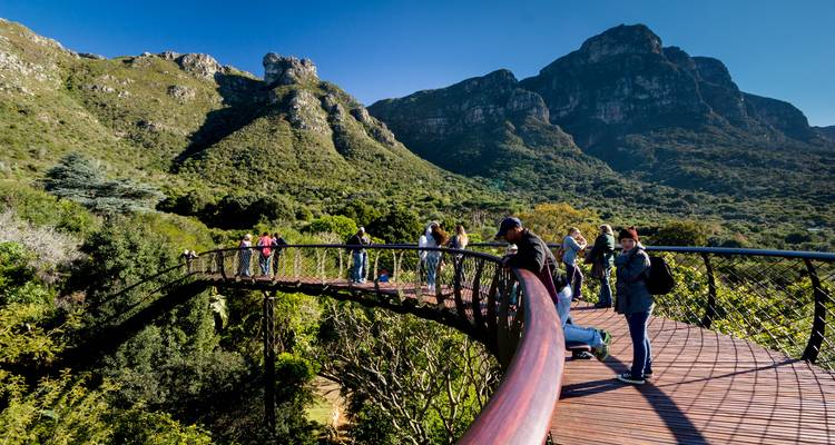 Menschen, die auf einem erhöhten Gehweg mit Bergen im Hintergrund gehen.