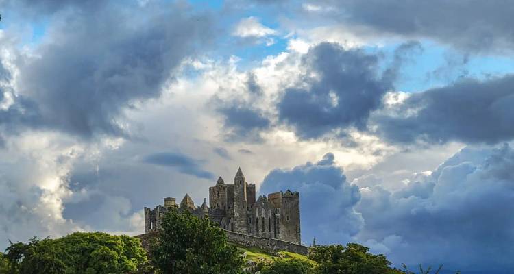 Dramatic view of the Rock of Cashel castle silhouetted against a stormy sky with sunlit breaks.