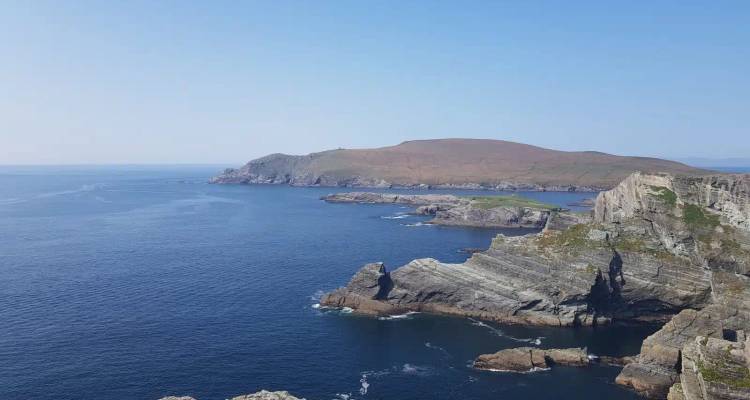 Rocky Irish headlands jut into deep blue Atlantic waters under a clear sky.
