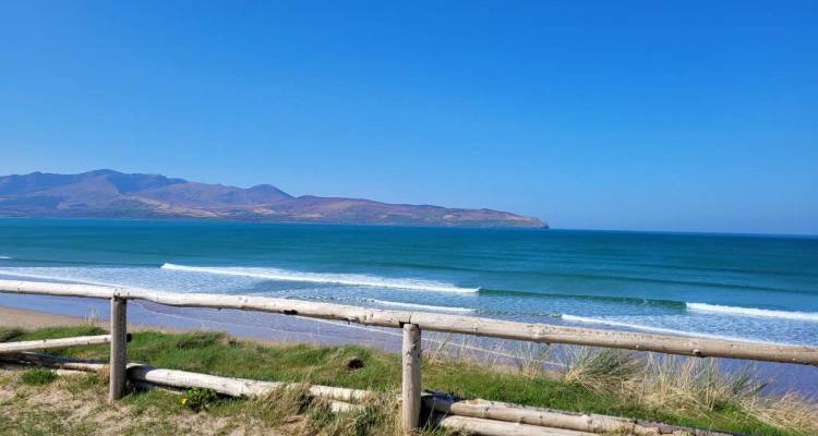 Wide sandy beach with turquoise waves rolling in and distant mountains along Ireland’s coast.