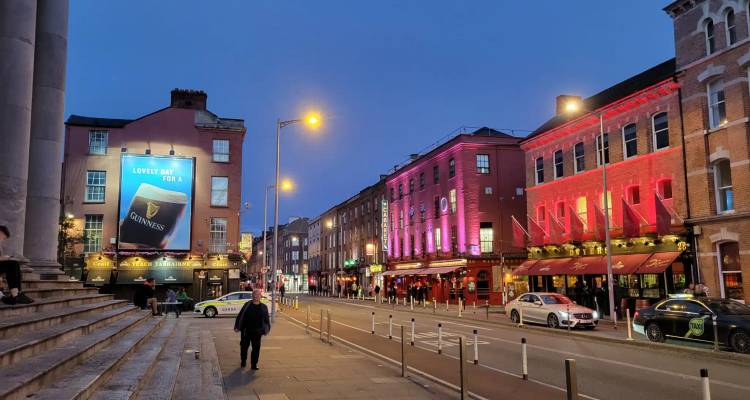 Vibrant evening street scene in Dublin with lit pubs, pedestrians and taxis under a twilight sky.
