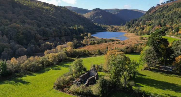 Autumnal valley with a tranquil lake, patchwork forest and the ruins of an old stone cottage in the foreground.