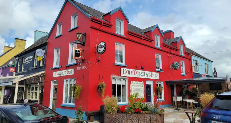 Bright red Irish pub with colorful neighbouring buildings under a patchy blue sky.