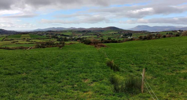 Green pastoral fields with distant rolling hills beneath a sky of broken clouds.