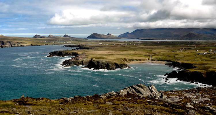 Vue panoramique côtière avec falaises, océan et collines lointaines.