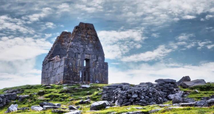 Weathered stone church ruins top a grassy hill against a dramatic cloudy sky.