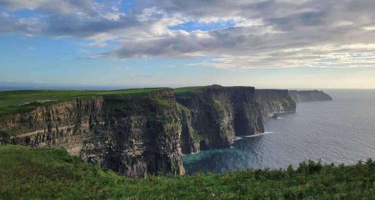 A panoramic view of towering sea cliffs backed by green fields and turquoise water below.