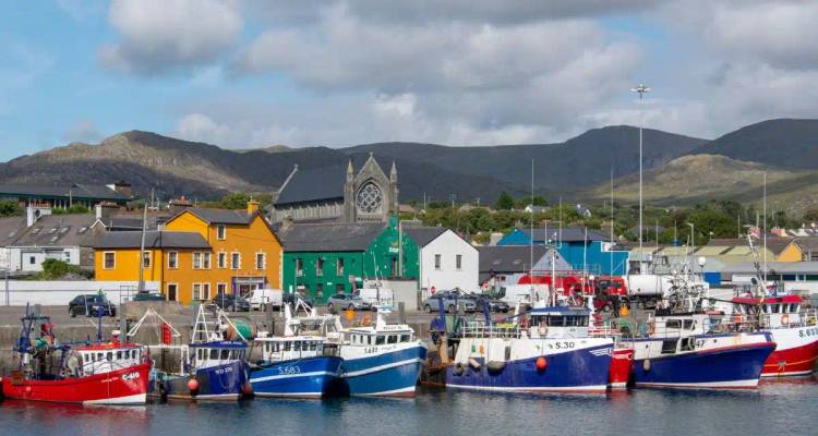 Colorful fishing boats moored at a lively harbour lined with bright houses and a church backdrop.