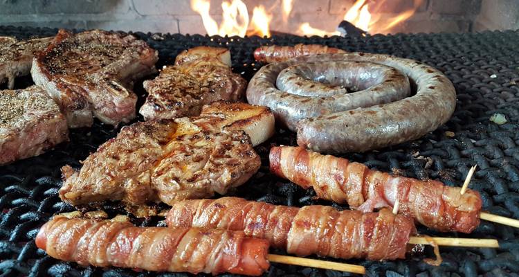 Grillrost mit verschiedenen Fleischsorten, die über Flammen garen.