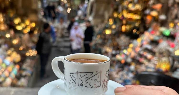 Tasse de café tenue en l'air avec un marché animé en arrière-plan.