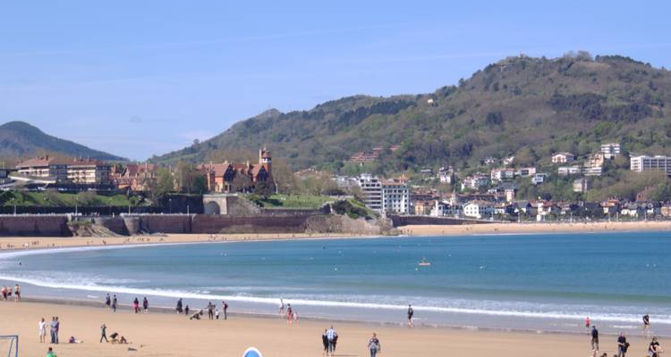 Frente de playa con personas y paisaje urbano distante y colinas
