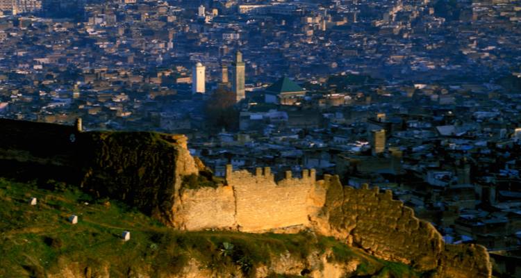 View of a historic city at dusk with fortified walls in the foreground.