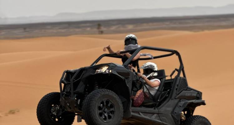 Two people driving a buggy on sand dunes.