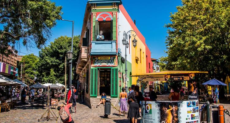 Rue piétonne animée à Caminito avec des bâtiments colorés, des étals en plein air et des touristes qui flânent sous un ciel dégagé
