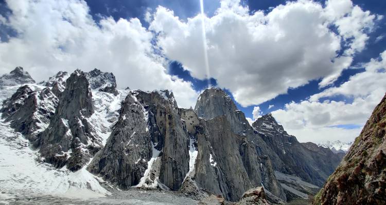 Amplio muro de agujas de roca con rayo de sol atravesando las nubes sobre un glaciar alpino