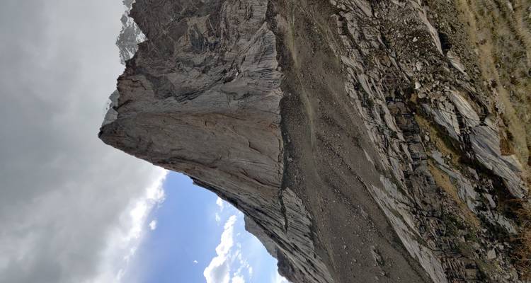 Pináculo rocoso empinado bajo un cielo melancólico con pendientes de derrubios que ascienden por la cara de la montaña