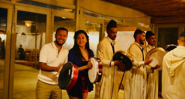 Koppel dat framesdrums bespeelt samen met lokale muzikanten in traditionele kleding binnen woestijnkamp