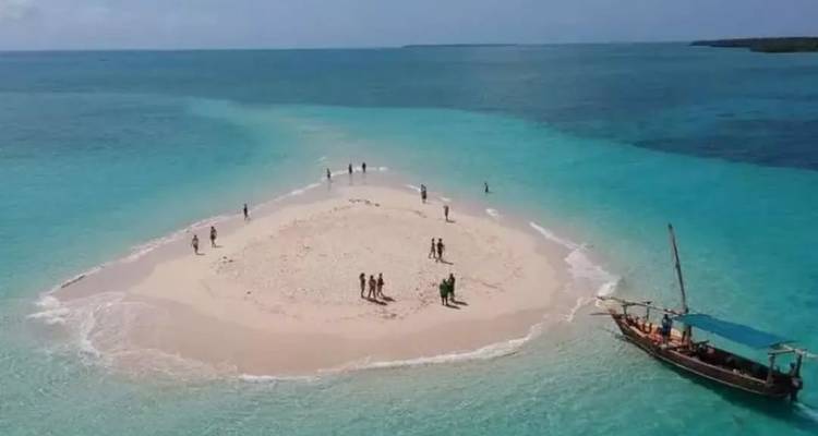Petite île sablonneuse avec des gens et un bateau traditionnel dans des eaux bleues.