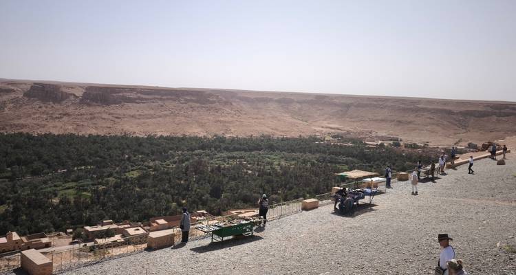 Un paysage avec une vue sur le désert, une oasis verte, et plusieurs personnes debout sur un sentier.