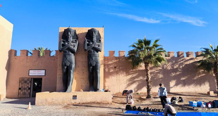 Deux grandes statues devant un bâtiment avec des palmiers et des personnes à proximité.