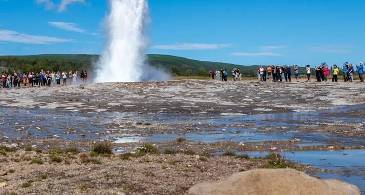 Personas observando la erupción de un géiser en un campo.