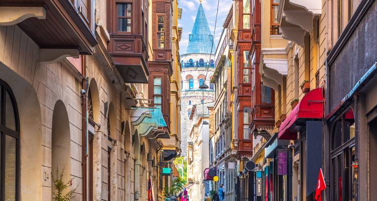 Vista de calle concurrida en Estambul, con tiendas coloridas y vibrantes y una torre histórica a lo lejos.