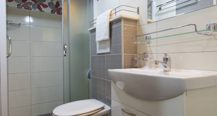A bathroom with a shower, toilet, and sink next to a tiled wall.