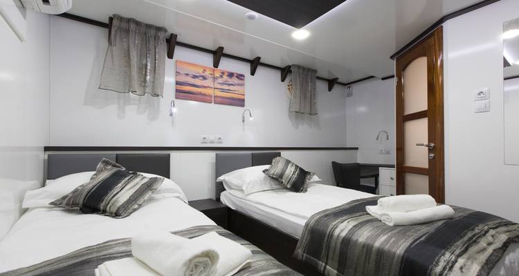 A small cabin with single beds, bedside lamps, and folded towels.