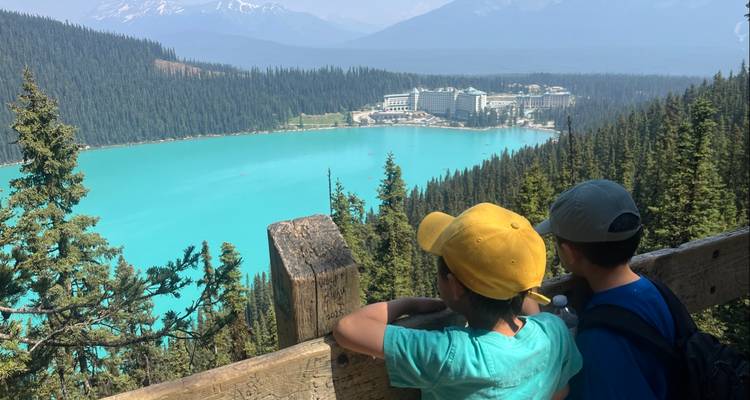 Two children looking at a turquoise lake and a resort in the distance.
