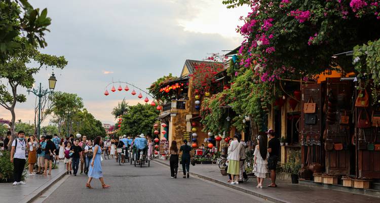 Belebte, mit Laternen gesäumte Straße in Hoi An, gefüllt mit Fußgängern, Fahrrädern und blühenden Bäumen.