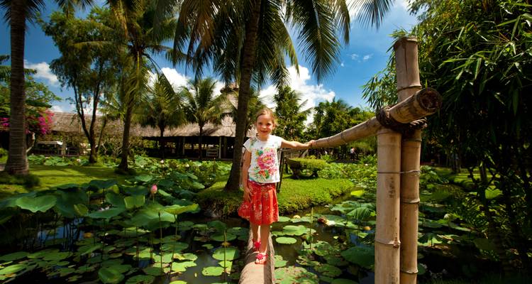 Enfant debout sur un pont en bois au-dessus d'un étang avec des fleurs de lotus.