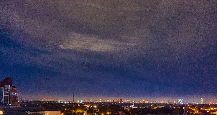 Vue nocturne du paysage urbain avec des lumières dispersées sous un ciel nuageux.