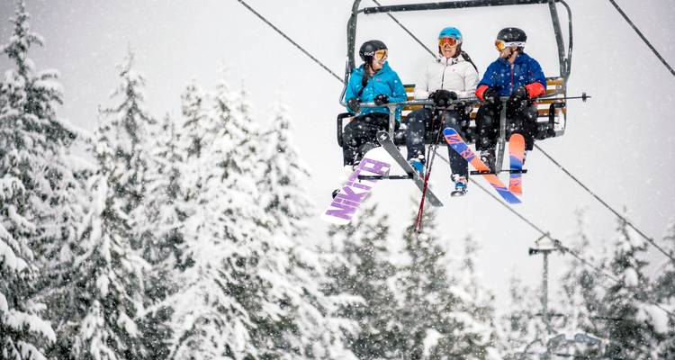 Trois personnes sur un télésiège au milieu d'une forêt enneigée.
