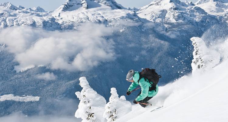 Un skieur descendant une pente avec des montagnes au loin couvertes de neige.