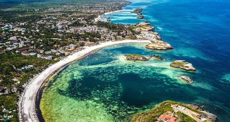 Vue aérienne d'une ville côtière avec un littoral incurvé et un océan bleu clair.