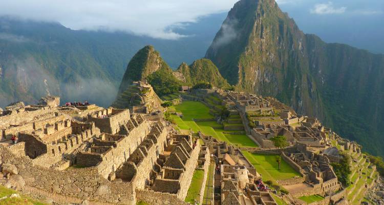 Ikonische Aussicht auf die Ruinen von Machu Picchu, die auf einem grünen Bergrücken inmitten nebelverhangener Andengipfel thront.