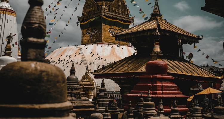 A stupa with fluttering prayer flags against a cloudy sky.